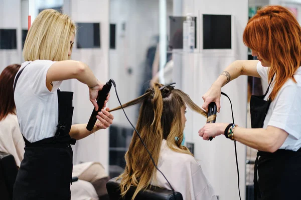 Dos peluqueros peinando un cabello de cliente femenino en el salón de belleza. —  Fotos de Stock