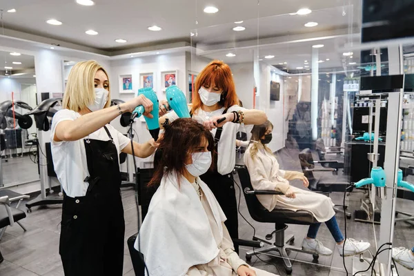Dos estilistas profesionales secando y peinando el cabello de un cliente en la peluquería. —  Fotos de Stock