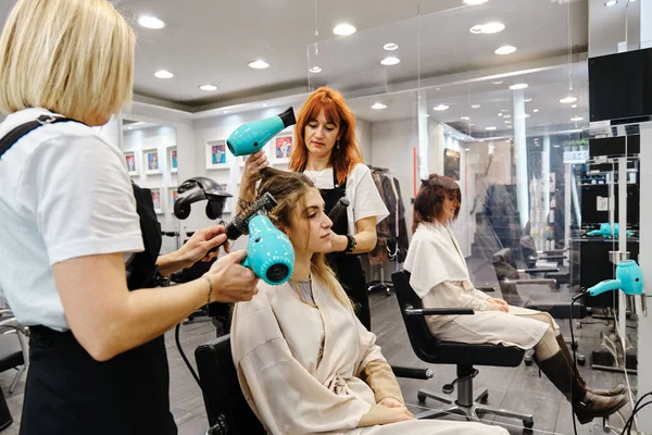 Dwóch profesjonalnych stylistów stylizujących włosy młodej kobiety w salonie piękności. — Zdjęcie stockowe