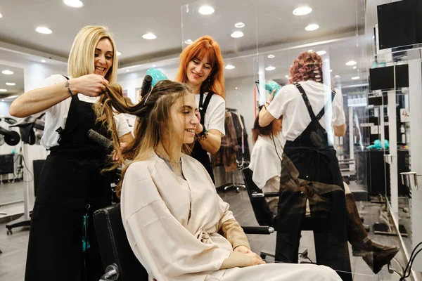 Profesjonalni styliści czesający włosy młodej kobiety w salonie piękności. — Zdjęcie stockowe