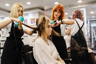 Güzellik salonunda genç bir kadın için saç stili yapan profesyonel stilistler..