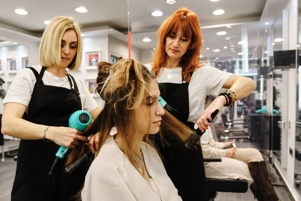 Dos peluqueros haciendo un peinado para una clienta femenina en el salón de belleza. —  Fotos de Stock