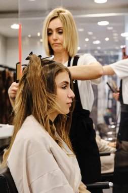 Profesyonel stilist, kuaförde saç stili yaparken müşterinin saçını düzeltiyor..