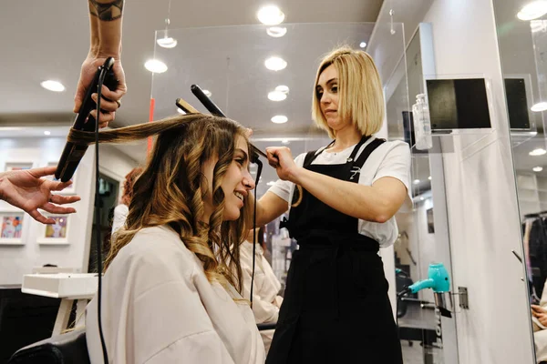 Dos peluqueros haciendo un peinado a un cliente en un salón de belleza. —  Fotos de Stock