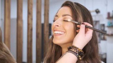 Güzellik salonunda makyajını yaptırırken gülümseyen mutlu kadın..