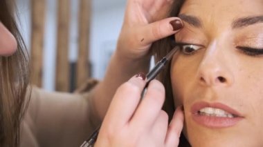 Profesyonel bir makyajcının müşterisine göz kalemi sürerken yakın plan görüntüsü.
