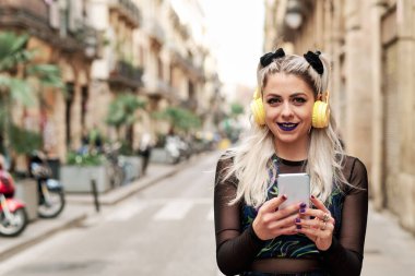 Sokakta cep telefonu ve kulaklıkla müzik dinlerken gülümseyen başka bir kadın..