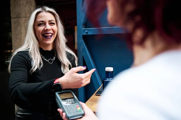 Woman making contactless payment with a smart watch at a coffee shop.