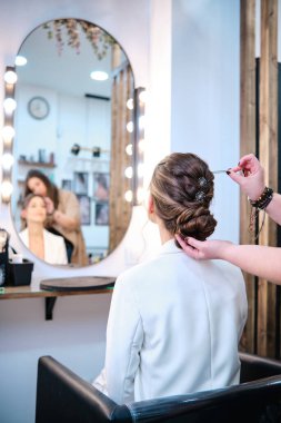 Profesyonel stilist güzellik salonundaki gelin saç stilinin detaylarını tamamlıyor ve ayarlıyor.