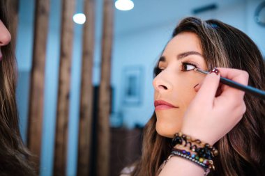 Profesyonel makyöz, güzellik salonunda makyajını yaparken müşterisine göz kalemi sürüyor..