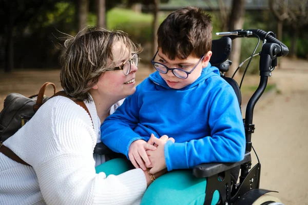 Niepełnosprawny chłopiec na wózku inwalidzkim, spacerujący z matką na świeżym powietrzu. — Zdjęcie stockowe