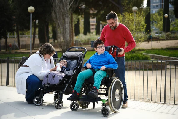 Mor och far njuter av en familjedag i parken med sitt barn och en handikappad son i rullstol. — Stockfoto