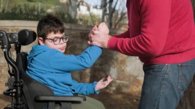 Tekerlekli sandalyedeki tetraplegialı genç çocuk dışarıda oynarken babasıyla eğleniyor..