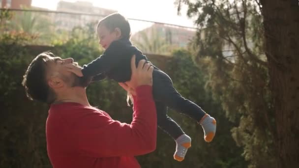 Happy man having fun and playing with his little son while holding up him in the air outdoors. — Stock Video