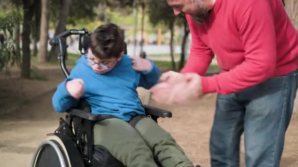 Сын с тетраплегией в инвалидном кресле и его отец наслаждается днем на открытом воздухе в парке. — стоковое видео