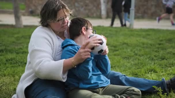 Chico con tetraplejia divirtiéndose con su madre mientras juega con una pelota de fútbol en el parque. — Vídeo de stock