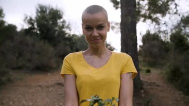 Doğada ayakta duran bir kadın genç yeşil bitkiyi kameraya gösteriyor..