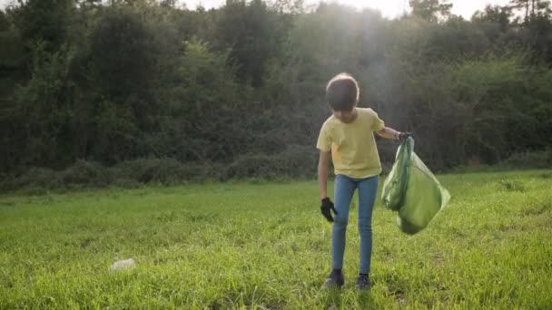 Young girl and her mother picking up garbage into trash plastic bag while cleaning up nature. — ストック動画