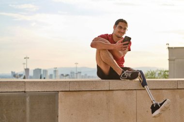 Engelli bir adam cep telefonunu kullanıyor ve dışarıda dinlenirken gülümsüyor..