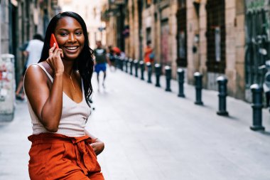 Gülümseyen Afrikalı Amerikalı kadın sokakta telefonda konuşuyor..