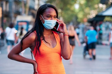 Sokakta dikilirken telefonda konuşan maskeli Afrikalı Amerikalı kadın..