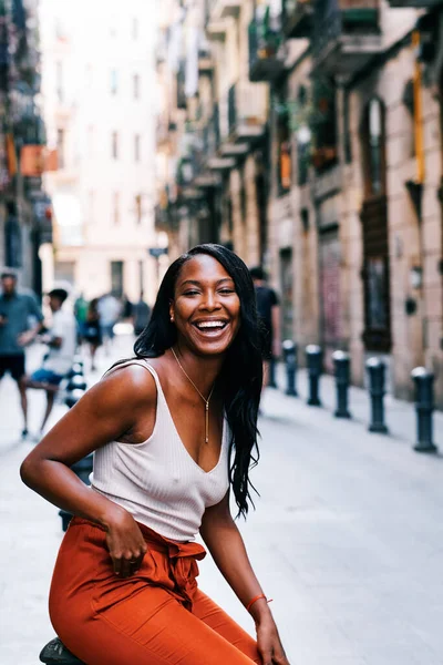 Genç Afrikalı Amerikalı kadın kameraya bakıyor ve şehir sokaklarında gülümsüyor..