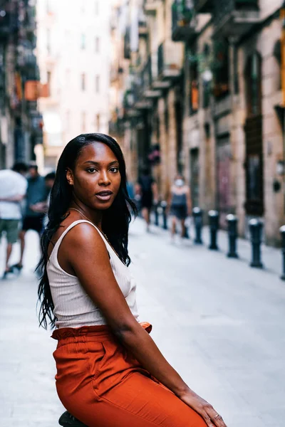 Afro-Amerikalı bir kadın sokakta otururken kameraya bakıyor..
