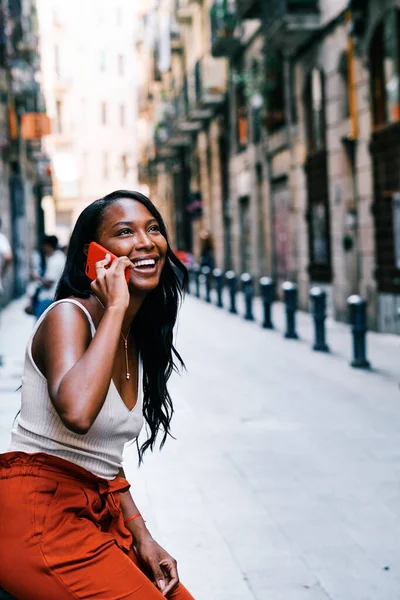 Smiling young woman talking on the phone while sitting outdoors on the street. — Stock Fotó
