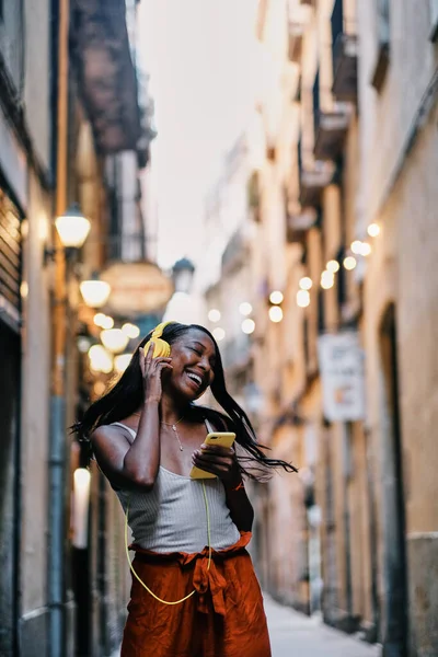 Happy woman enjoying listening to music with a mobile phone and headphones outdoors on the street. — Stock Fotó