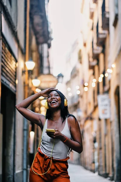 Joyful African American woman listening to music with mobile phone and headphones outdoors. — Stockfoto