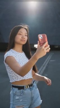 Kendine güvenen genç bir kadın dışarıda beklerken cep telefonuyla selfie çekiyor..