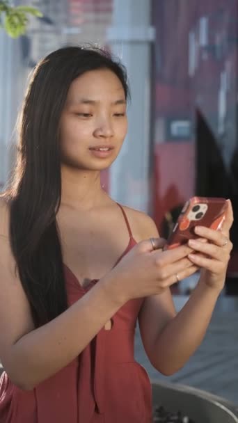 Jovem mulher asiática rindo enquanto lê uma mensagem em seu telefone celular. — Vídeo de Stock