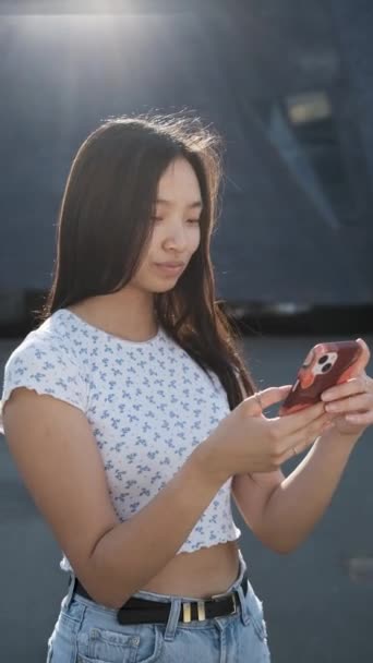 Mladá asijská žena pomocí svého mobilního telefonu při stání venku. — Stock video