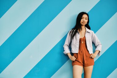Kendine güvenen genç Asyalı kadın dışarıda çizgili bir duvara poz verirken kameraya bakıyor..