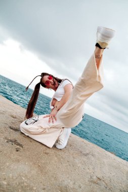 Neşeli bayan dansçı arka planda denizle dans ederken poz veriyor. Serbest stil ve sokak dansı konsepti.