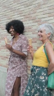 Mature women talking and eating ice cream while relaxing outdoors on the street on a summer day. Summer concept.
