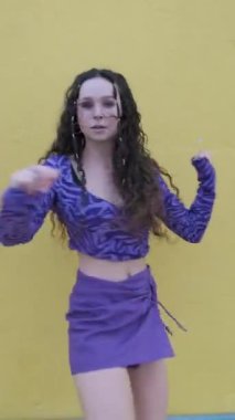 Dişi hip hop dansçısı, sarı bir duvara karşı dans ederken kameraya bakıyor. Müzik, dans ve gençlik kültürü.