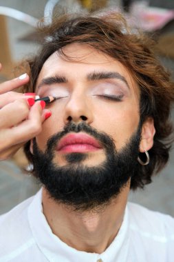 Close up view of a makeup artist applying eyeliner to a man while doing his makeup. lgbt concept.