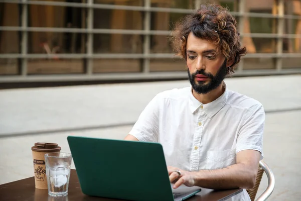 Businessman with makeup using a laptop while sitting in an outdoor coffee shop. Lgbti and business concept.