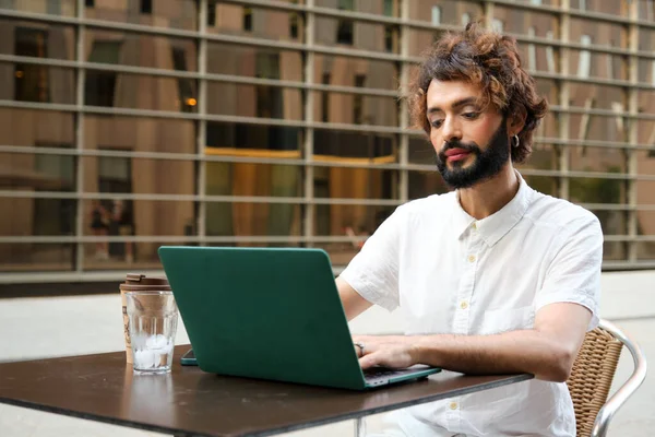 Businessman with makeup working on laptop while sitting in outdoor cafe. Lgbti and business concept.