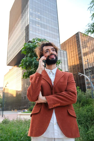 Businessman with makeup looking away and smiling while talking on the phone in the financial district. Lgbti concept.
