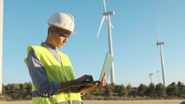 Female engineer using a laptop while working outdoors at a wind turbine farm. Sustainable lifestyles, renewable energy and technology concept.