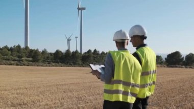 Two engineers check the wind turbine system together while working in wind farm. Sustainable lifestyles, renewable energy and technology concept.