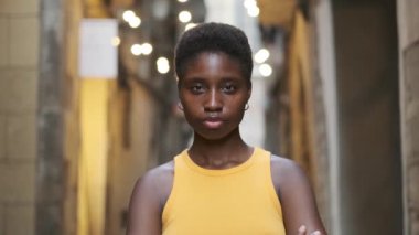 Young black woman looking at the camera and smiling while standing outdoors on the street.