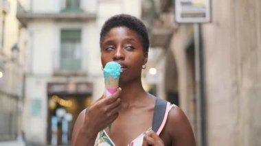 Woman enjoying eating an ice cream while standing on the street on a summer day.