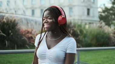 Young African American woman with vitiligo smiling while enjoying listening to music with headphones outdoors. Technology concept.