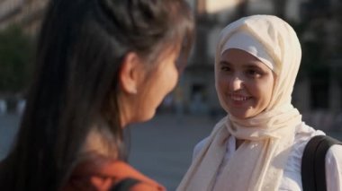 Genç bir Arap kadının tesettürlü fotoğrafı. Sokakta bir arkadaşıyla konuşurken gülümsüyor..