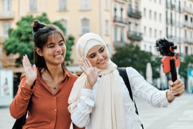 Çok ırklı arkadaşlar sokakta cep telefonuyla dolaşırken gülümseyip el sallıyorlar. Teknoloji ve sosyal ağlar kavramı.