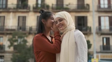 Genç Asyalı kadın sokakta dikilirken Arap arkadaşına bir sır fısıldıyor. Arkadaşlık kavramı.