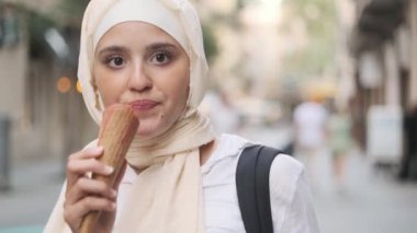Genç bir Arap kadın sokakta dondurma yerken kameraya bakıp gülümsüyor..